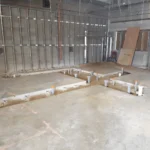 Construction site with exposed pipes and unfinished walls.