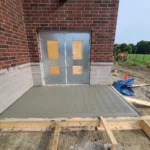 Fresh concrete sidewalk outside building entrance.