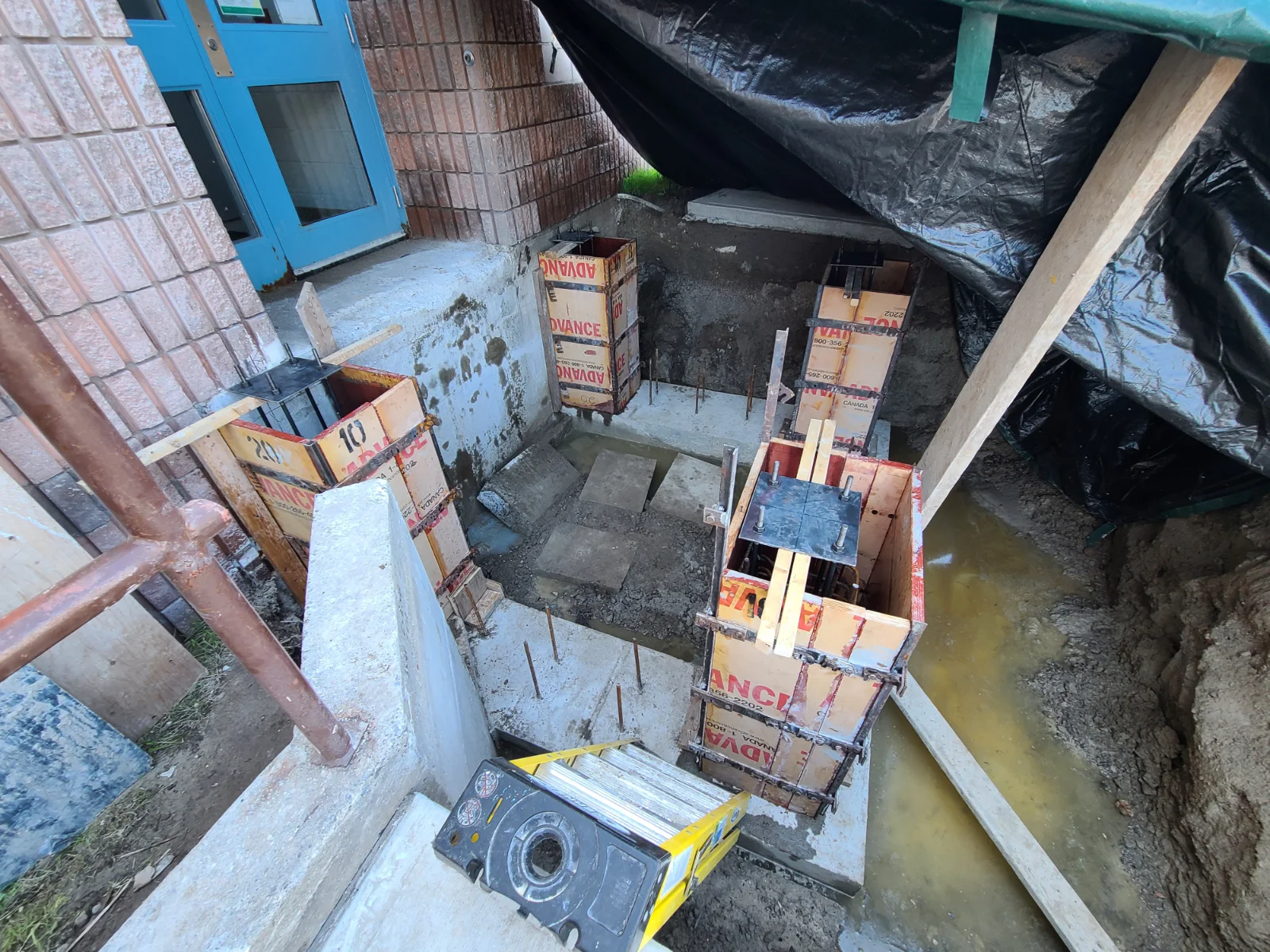 Construction site with concrete forms and muddy ground.