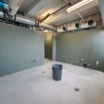 Construction site with green drywall and pipes.