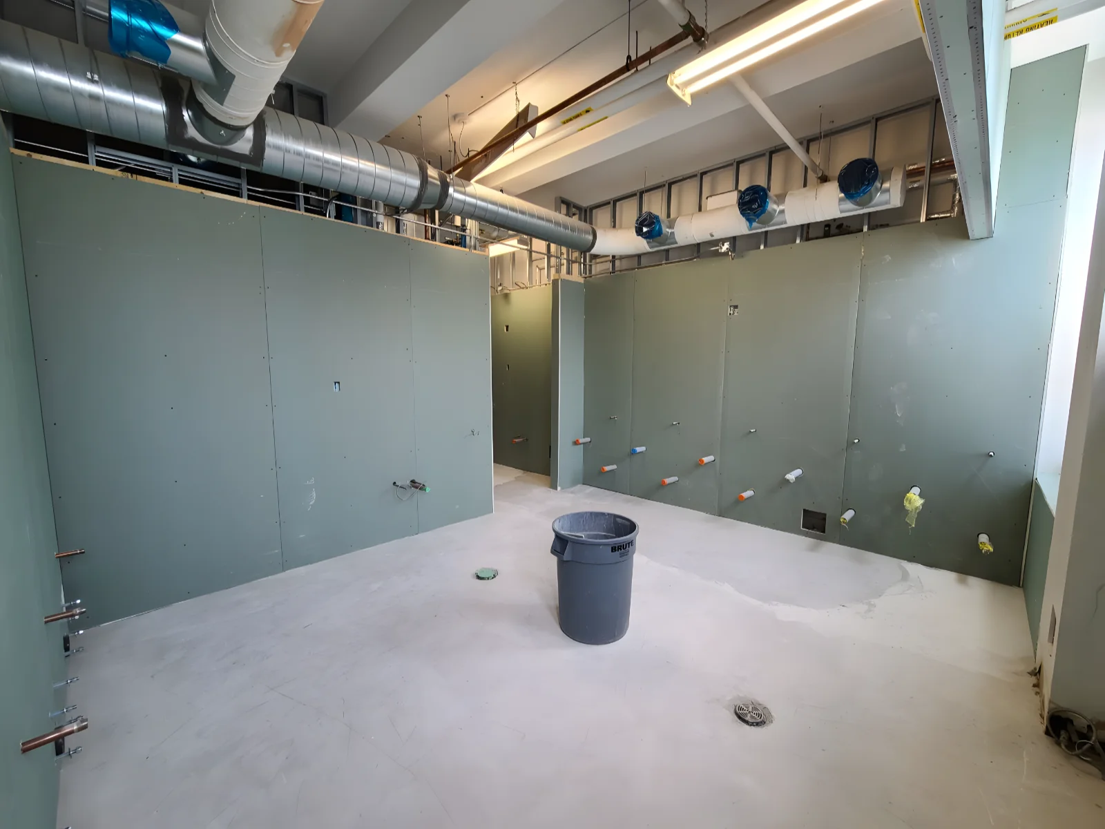 Construction site with green drywall and pipes.