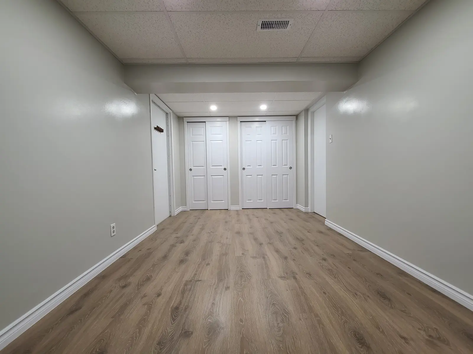 Spacious empty basement with wooden flooring and white doors.